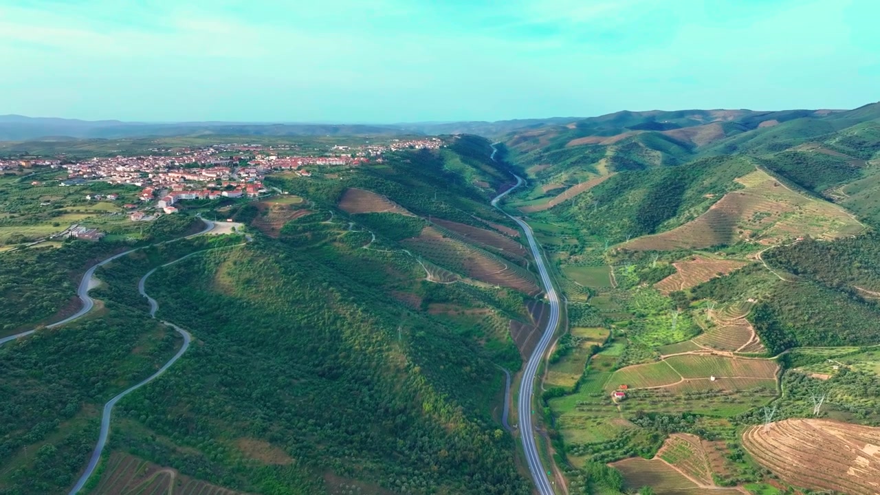 Vedute aeree della Valle del Douro in Portogallo mostrano vigneti a terrazze e una strada panoramica nella valle. Linee di trasmissione elettrica attraversano il paesaggio energetico verde. Aree rurali circondano i vigneti.