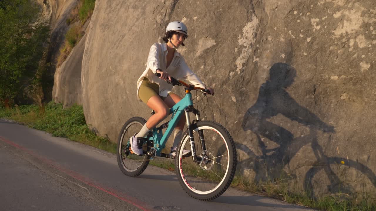 Mujer ciclista deportista con casco en una carretera al atardecer.
