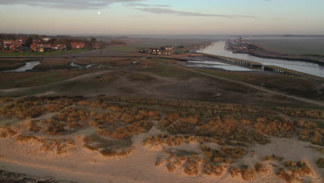 rising flight from walberswick beach looking towards walberswick and southwold harbour, suffolk at sunrise with the moon and mist