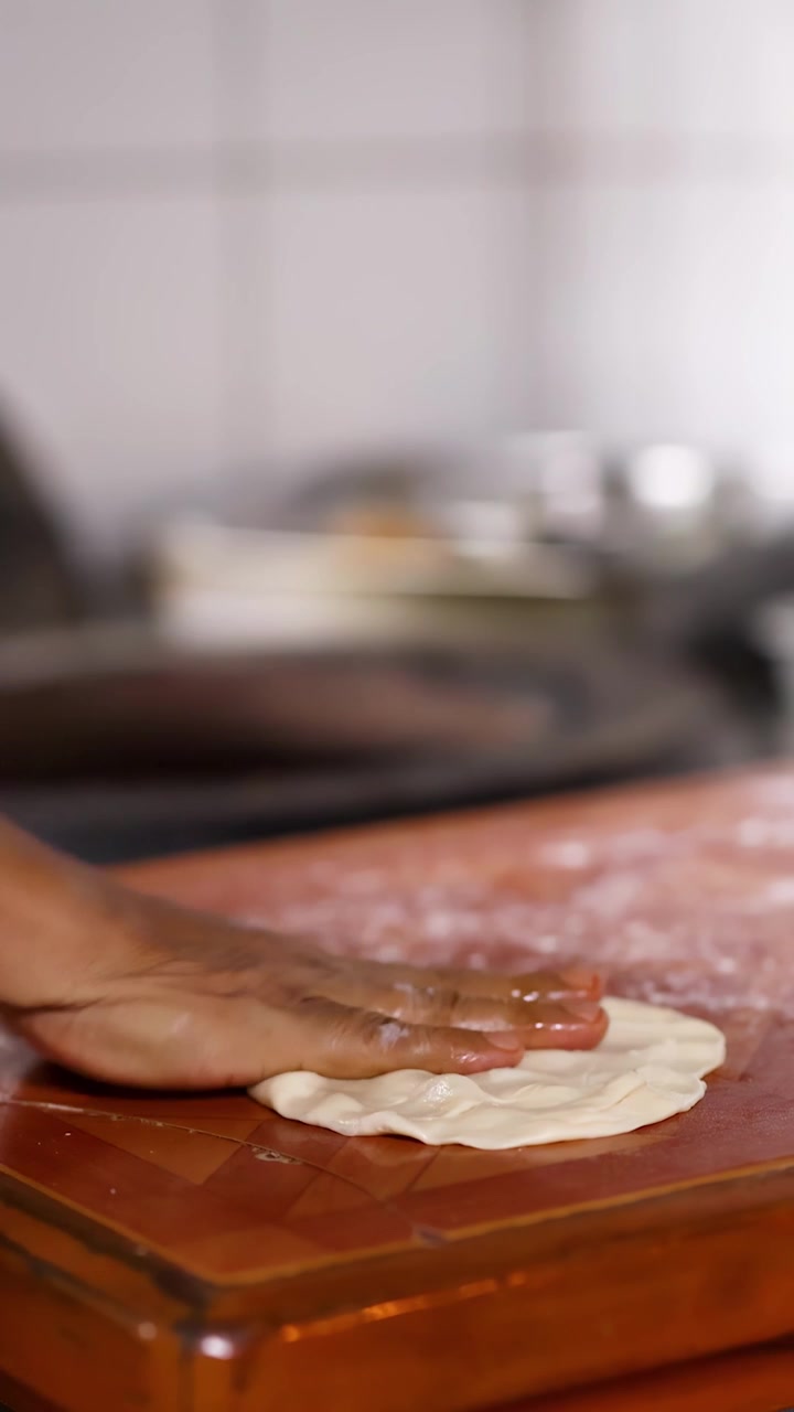 Close-up of hands skillfully preparing flatbread dough on a wooden surface in a kitchen.