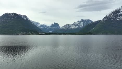 city of andalsnes in norway seen from across the fjord - aerial rising above treetops and ascending towards andalsnes city with mountain romsdalshornet in background