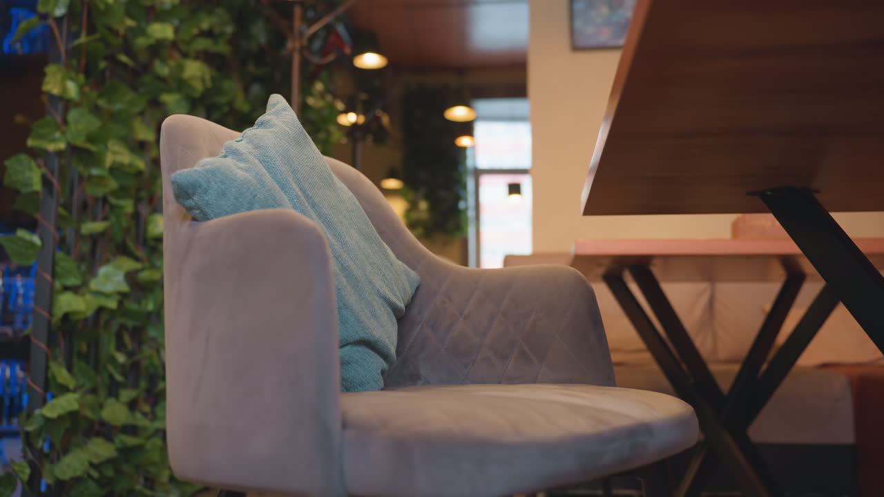 Beautiful view of cozy bar interior featuring cushioned lounge chairs with soft pillows, wooden accents, vertical green plant wall, and soft ambient lighting