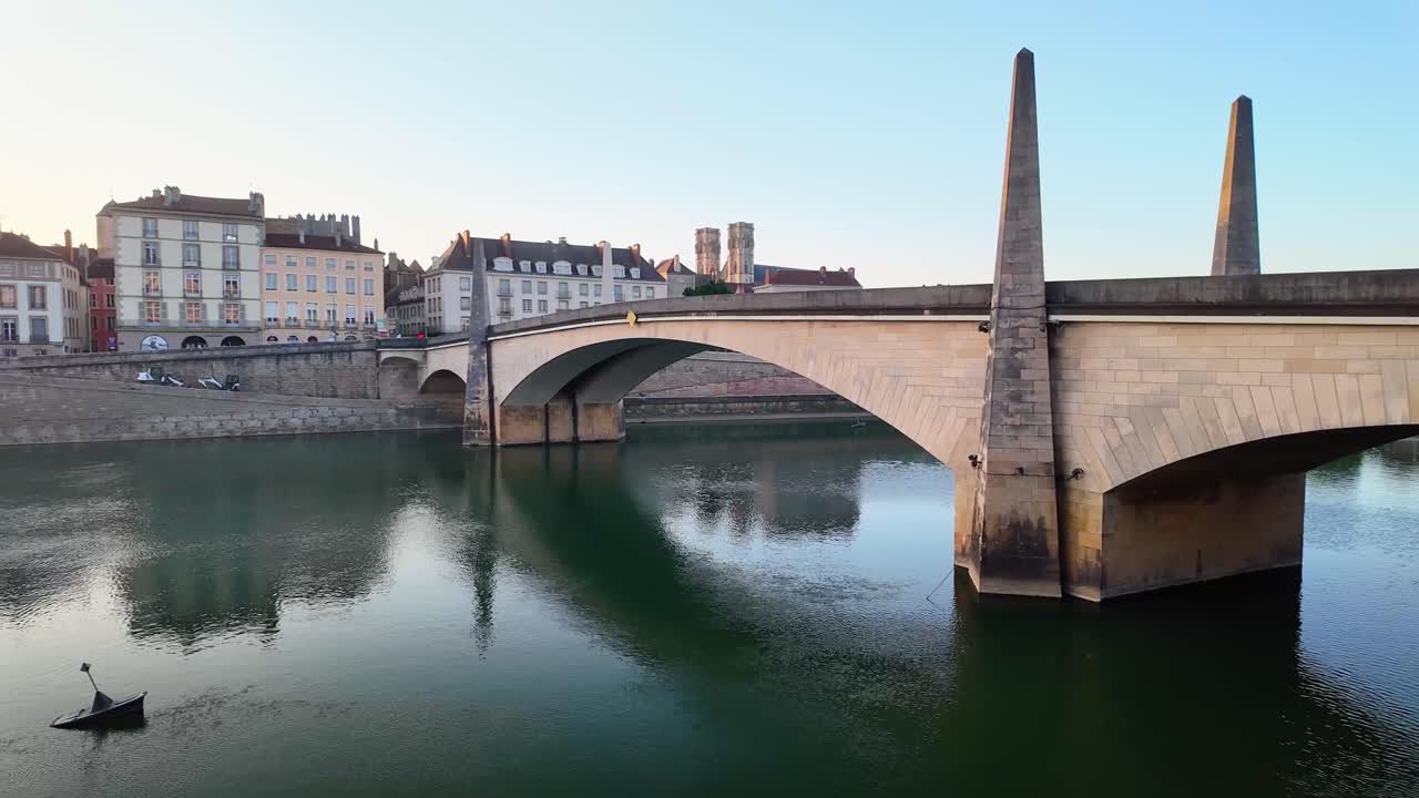 View of Pont Saint-Laurent from the riverbank in Chalon-sur-Saône, France. Stone arches, green river waters, and warm sunset light.