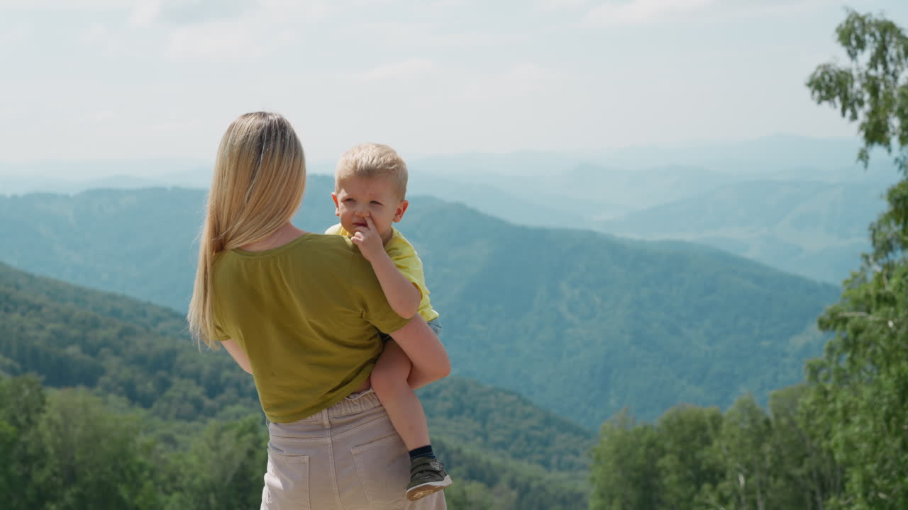 Liebende Mutter küsst Kleinkind vor großen Bergen.