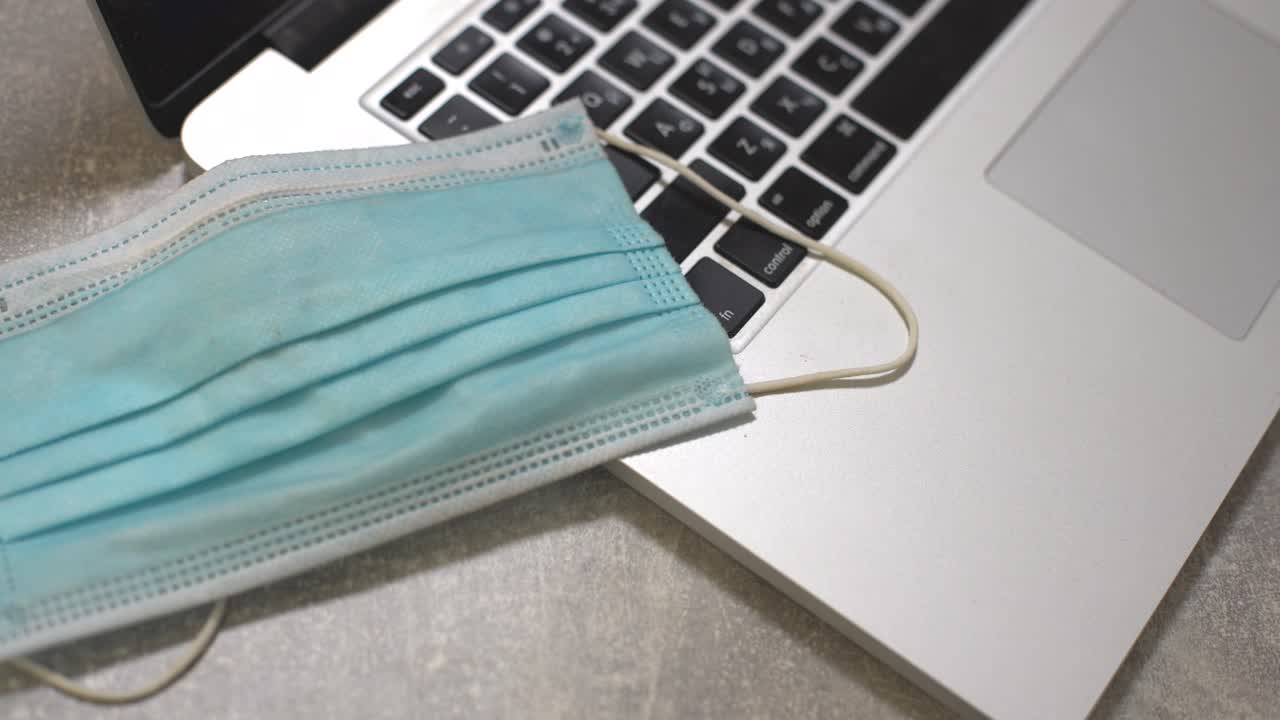 의료 얼굴 마스크, 노트패드 및 펜을 가진 노트북 컴퓨터와 함께 식탁에 커피 한 잔. 가정 설정. 집에서 일하는 개념.