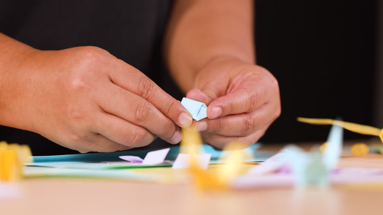 Primo piano di mani che usano forbici gialle per tagliare e piegare carta blu per origami