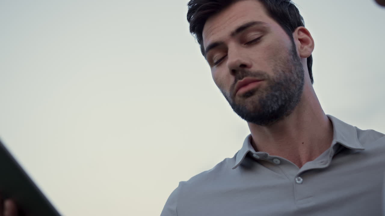 Hombre mirando la pantalla de una tablet al aire libre. Apuesto hombre hablando en línea en el campo de golf.
