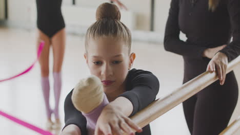 close up view of a gymnastic blonde girl rehearsing a posture at the ballet barre 1