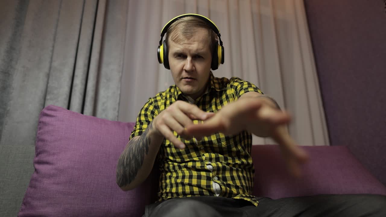 Uomo seduto sul divano ascolta musica dalle cuffie wireless e balla.