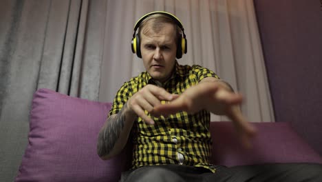 man sitting on the sofa listens music from wireless headphones and dances