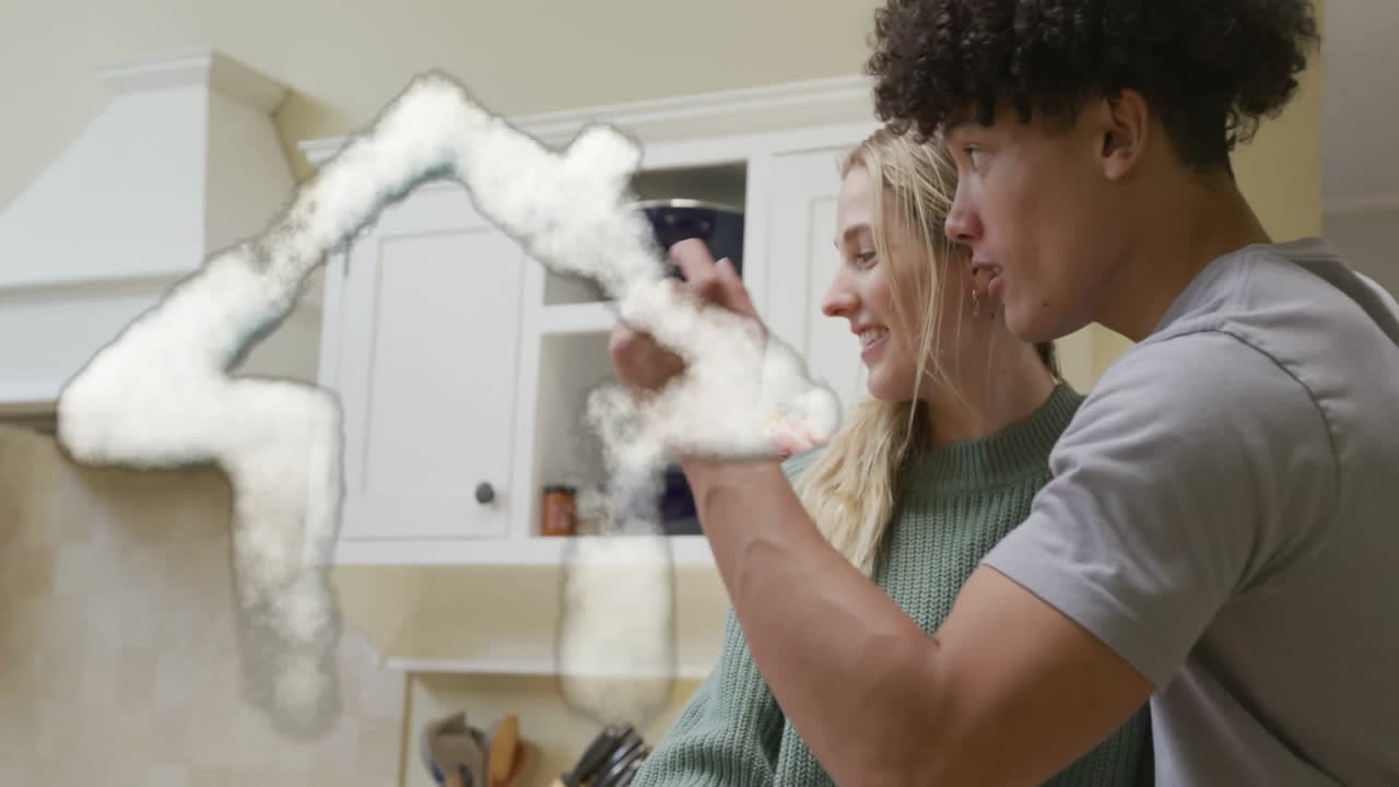 Animation of cloud house over happy diverse husband surprising wife with gift in kitchen