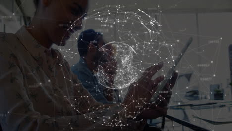 female colleague tapping tablet in tech office, male colleague observing data globe overlay