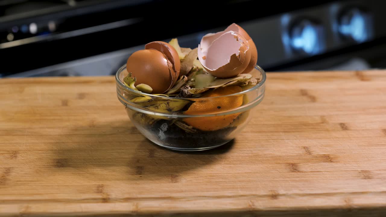 Compost material in a bowl in the kitchen on a cutting board, including eggshells, potato peels, fruit rines