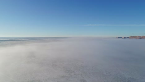 Aerial-moving-across-frozen-desert-with-low-lying-inversion-fog-on-ground,-4K