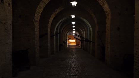 long corridor with arched stone walls inside medieval fortress of gjirkastra filled with guns and weaponry