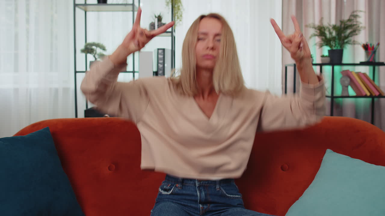 радостная молодая женщина показывает рок-н-ролл жест, прохладный знак танца радуется успеху дома