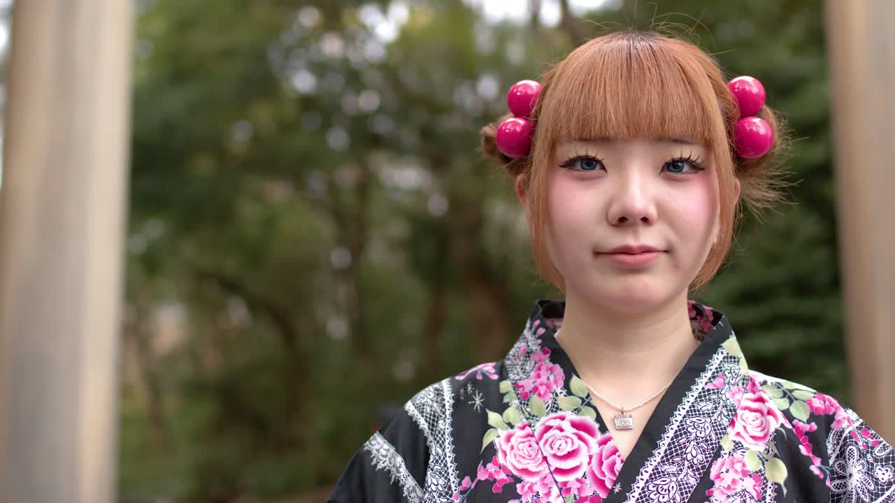 Una giovane donna giapponese in yukata tradizionale sta in piedi davanti a un grande cancello torii di legno.