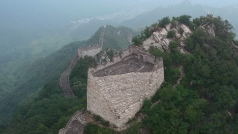 old deteriorated square lookout tower of great wall of china on top of mountain summit on a cloudy day