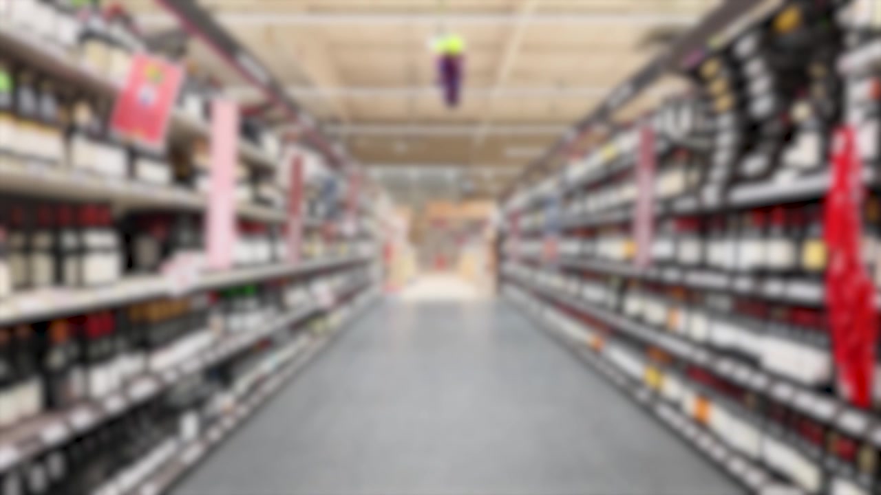 Out of focus camera moves forward through rows of wine bottles in a supermarket