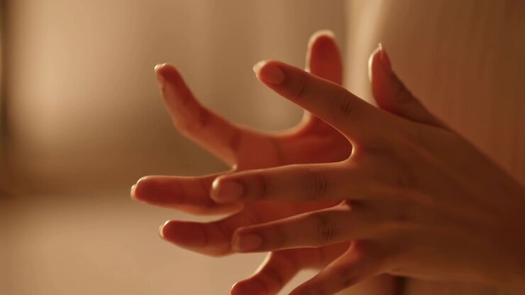 Vue rapprochée des mains et des doigts passant d'un contact doux à une posture ouverte et réceptive, avec les doigts écartés, les jointures courbées, des détails de peau douce, une lumière chaude, procurant une sensation de bien-être calme.
