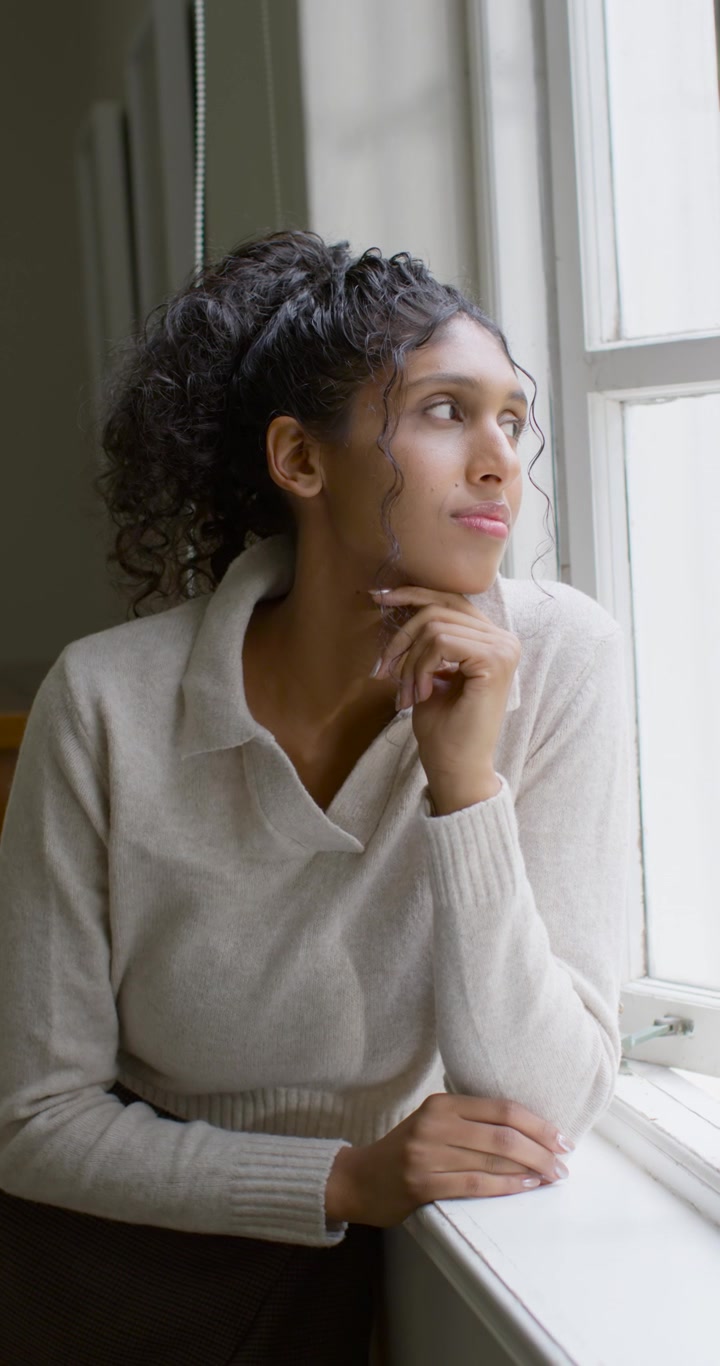 Vertical video: African American woman gazing out window, being prompted by soft light, reflecting