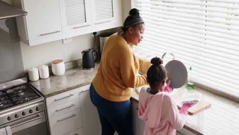 Happy-african-american-mother-and-daughter-washing-up-dishes-in-kitchen,-slow-motion