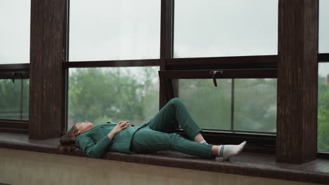 una mujer en un traje verde soñando despierto junto a una ventana.