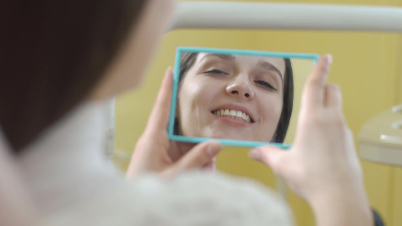 Mujer joven revisándose los dientes en un espejo en el dentista