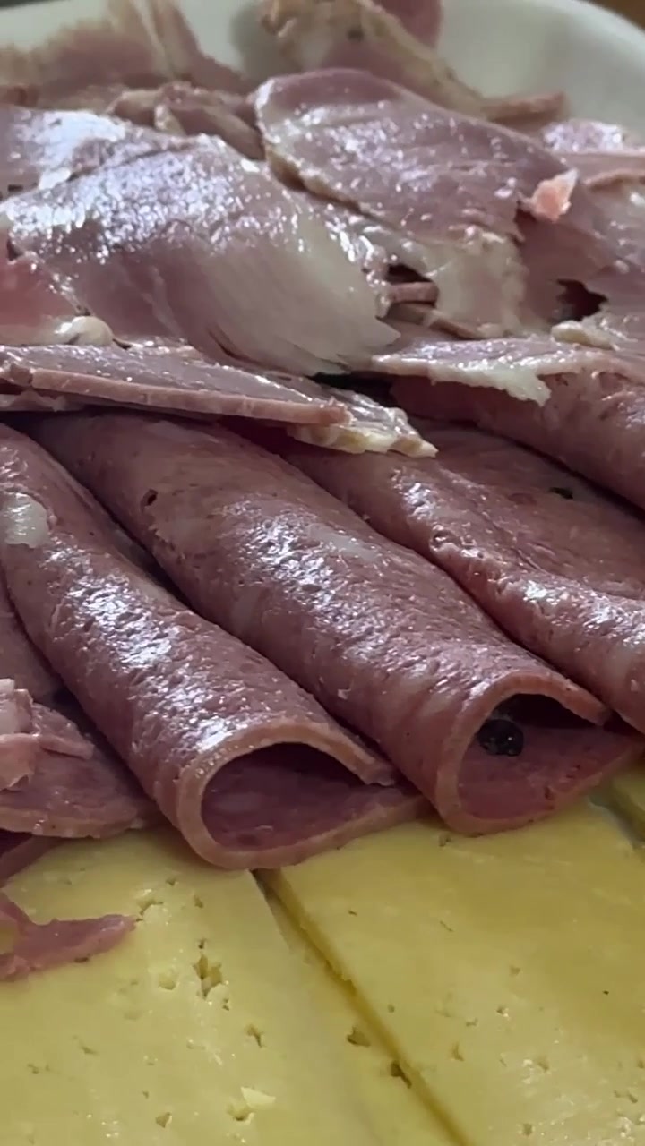 Formaggio a fette e affettato arrotolato serviti su un piatto con un giardino lussureggiante, scatto ravvicinato