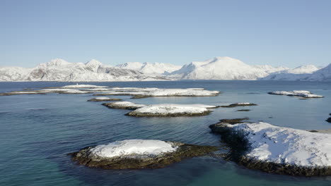 aerial view of small snow covered islands along the shallow arctic coastline of norway, forward motion