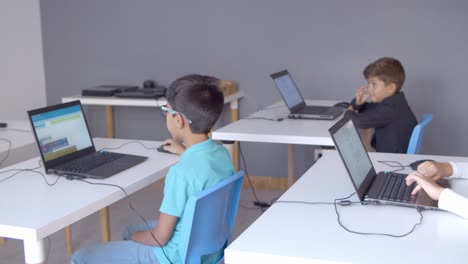 children sitting at desks with laptops in classroom