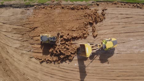 a bulldozer and a dumptruck work together unloading and flattening excess amounts of earth and soil