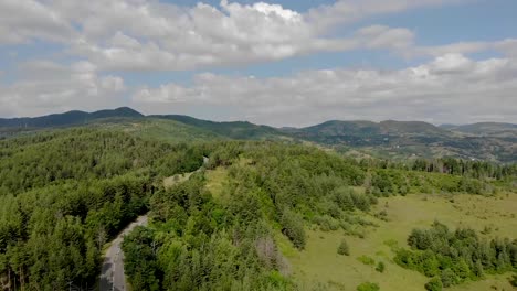 Fliegen-über-Eine-Leere-Straße,-Umgeben-Von-Bäumen-In-Den-Bergen-Mit-Wolken-Am-Himmel