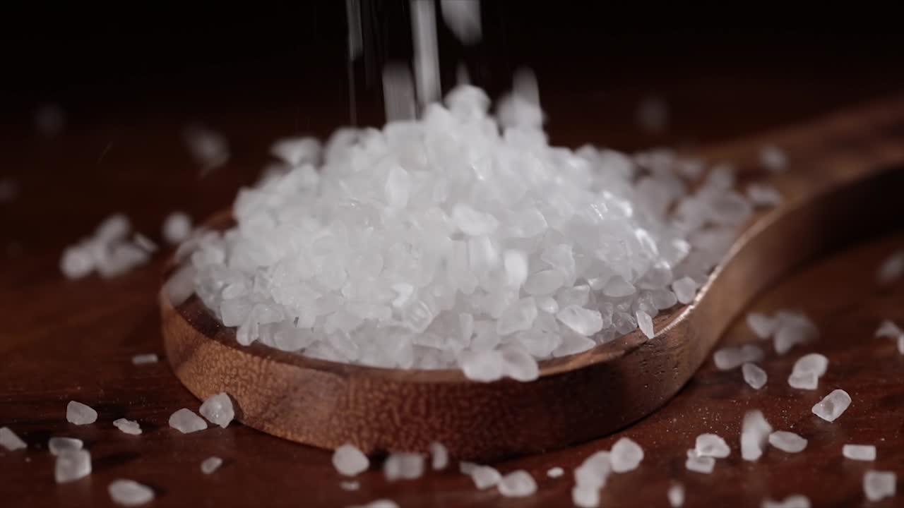Sea salt crystals closeup in wooden spoon on a kitchen table.
