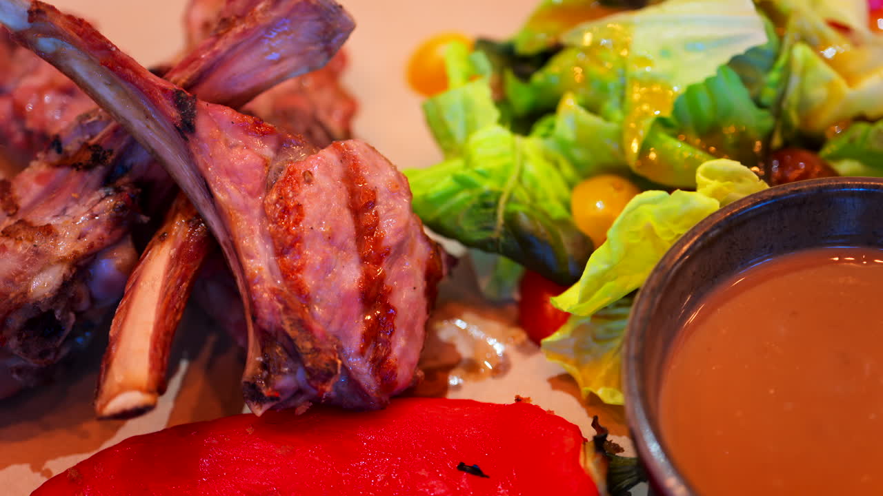 Close up of lamb chops with sauce and a side salad on a plate at a restaurant