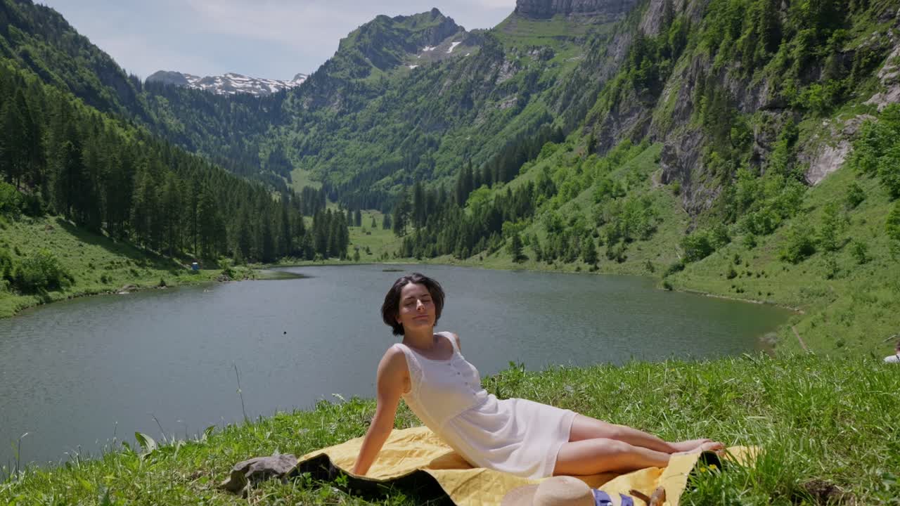 Brunette Model on blanket enjoying in valley in front of Talalpsee Lake in Switzerland. Slow motion close up.