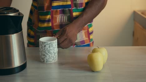 Hombre-Afroamericano-Vestido-Con-Tela-Kente-Vertiendo-Agua-Caliente-En-Una-Taza