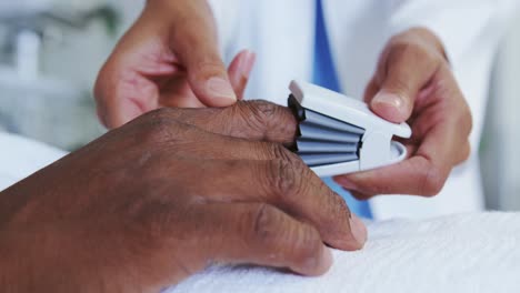 close-up of african american female doctor attaching pulse oximetry on male patient hand in the ward