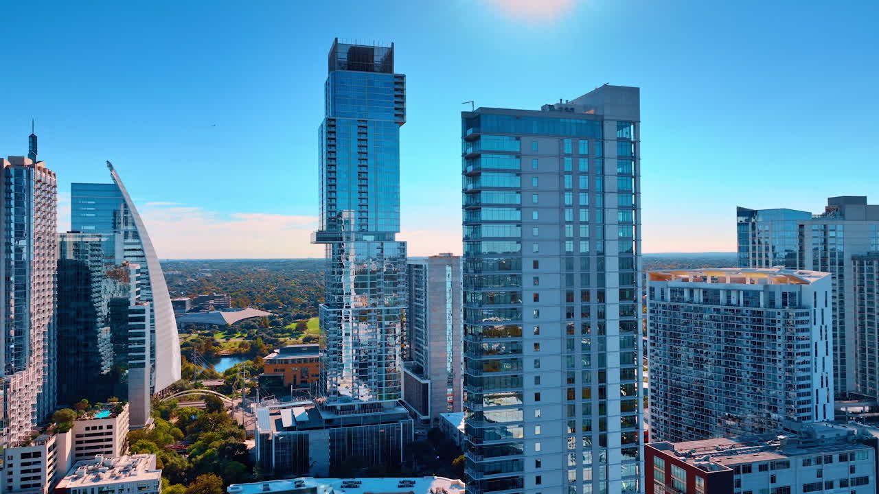 Austin, USA, 21 novembre 2025: Moderni grattacieli residenziali e per uffici contro un cielo azzurro e limpido. Veduta aerea all'altezza degli occhi di edifici a più piani in vetro e verde di un parco urbano sullo sfondo.