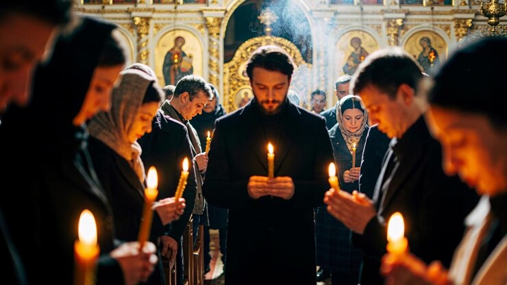 Leading priest in cassock holding taper candle in Eastern church aisle, incense rising