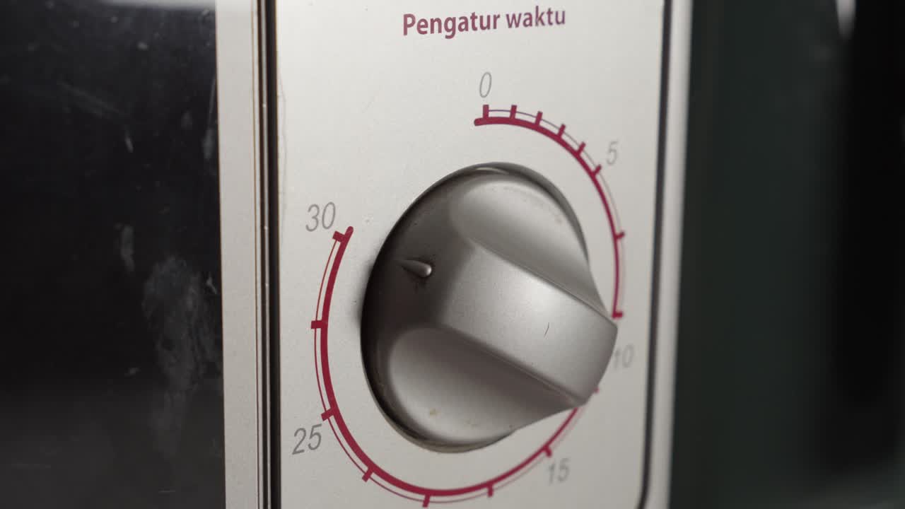 Mano che gira manualmente la manopola del forno a microonde elettrico, primo piano.