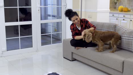 young woman strokes her dog because he afraid of vacuum-cleaning robot