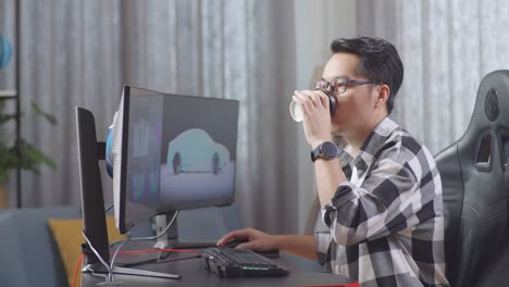 아시아 남성 자동차 디자이너가 스튜디오의 데스크 컴퓨터에서 ev 자동차의 3d 모델을 작업하는 동안 커피를 마시고 있는 측면 시각