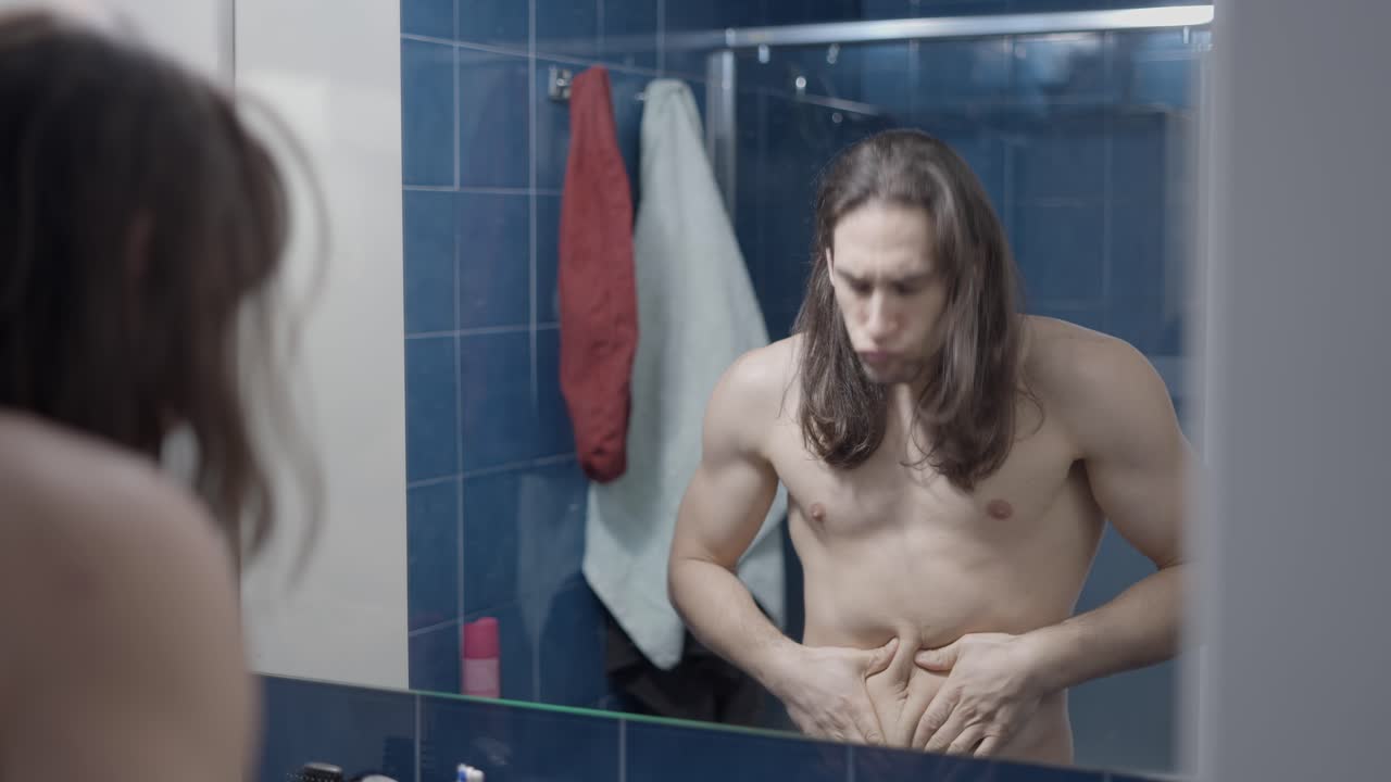 Man checking his stomach in the bathroom mirror