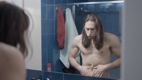 man checking his stomach in the bathroom mirror