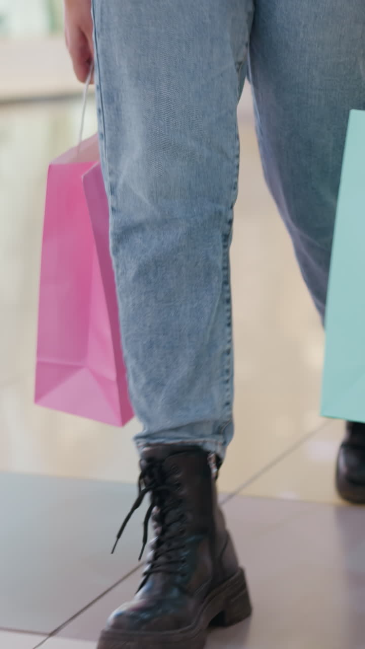 vista de la pierna de una mujer caminando en el centro comercial sosteniendo bolsas de compras con fondo borroso que muestra a otros compradores caminando, reflejando el ajetreado entorno comercial y el estilo de vida de la ciudad