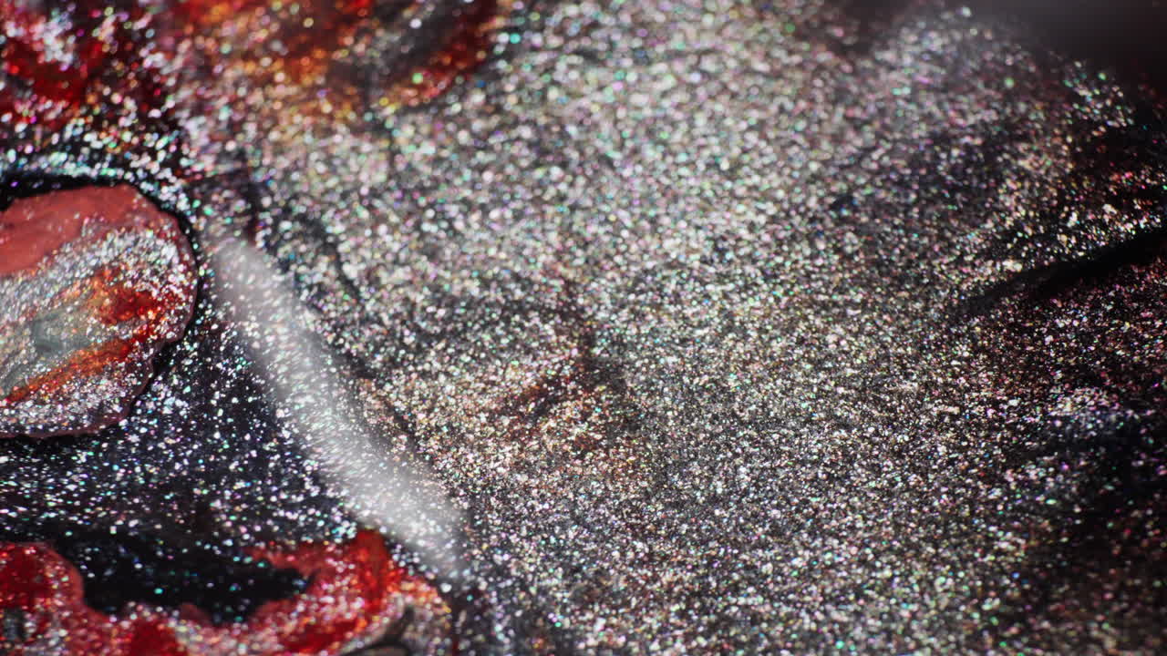 Macro shot of shimmering black, gray, and red inks interacting after a droplet falls off-screen, creating swirling textures and movement