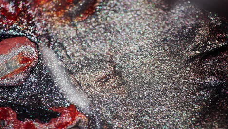 macro shot of shimmering black, gray, and red inks interacting after a droplet falls off-screen, creating swirling textures and movement