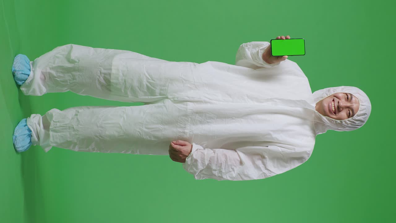 녹색 스크린 배경에 서 있는 동안 미소 짓고 녹색 화면 스마트폰을 보여주는 아시아 남성 과학자의 몸이 가득 차 있습니다.