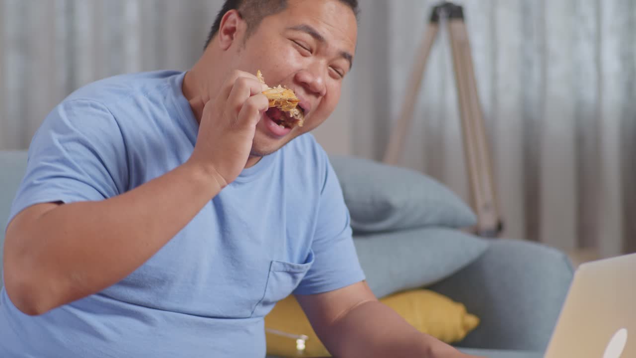집에서 거실에서 노트북에서 일하는 동안 김 을 먹고 패스트푸드를 먹는 한 아시아 남자의 클로즈업